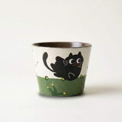Gemini_Generated_Image_mae0e0mae0e0mae0 KilnSongStudio handmade ceramic cat cup with a hand-painted black cat in a green spring garden, featuring a rustic speckled texture and Wabi-sabi design.